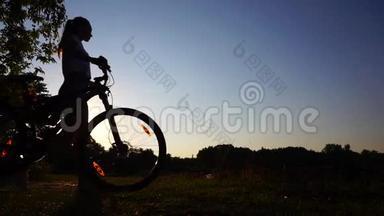 女孩骑自行车的剪影，扎着马尾辫，骑着自行车走路。 慢镜头拍摄日落